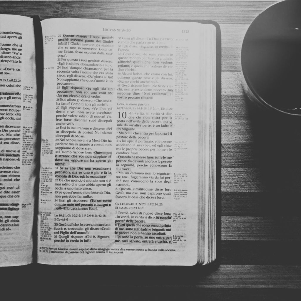 Open Bible and Coffee | Praying and Devotions About Faith Black and white photo of an open Bible next to a coffee cup on a wooden table, symbolizing praying and devotions about faith.
